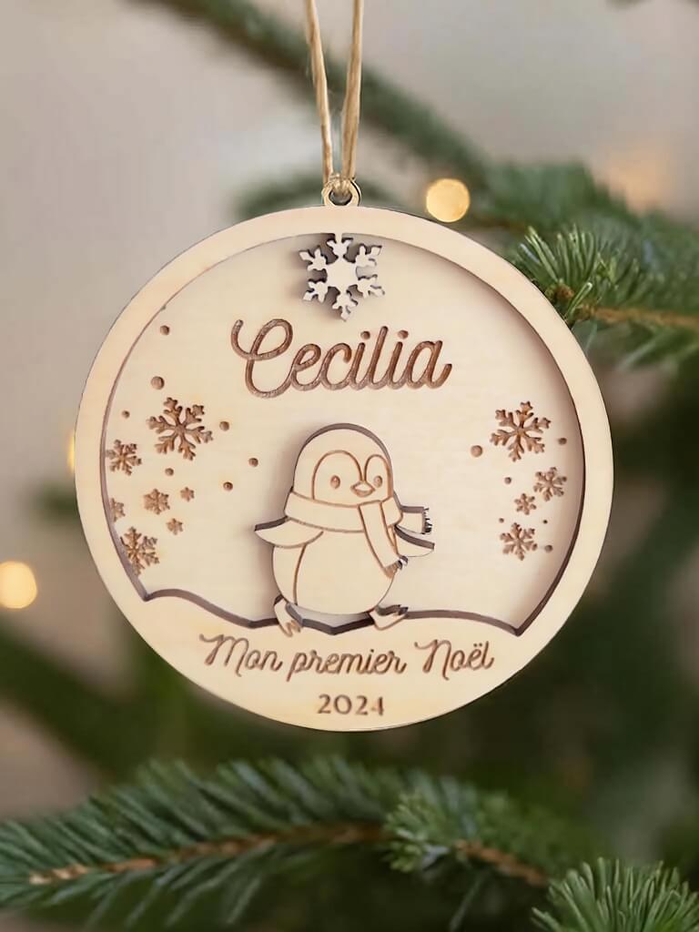 Boule de Noël en bois personnalisée motif Pingouin, suspendue dans un sapin décoré.