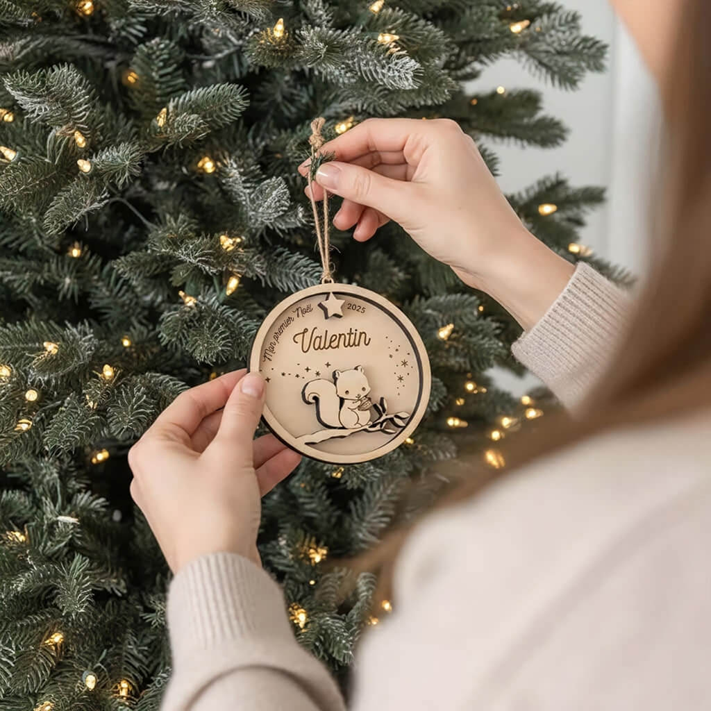 Suspension de Noël en bois motif Écureuil, accrochée au sapin par une main.