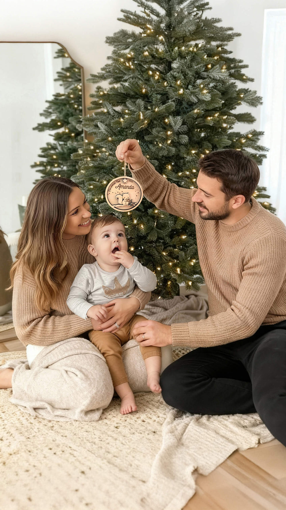 Famille devant le sapin tenant une boule de Noël personnalisée en bois pour le premier Noël de bébé